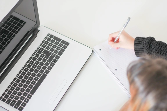 Woman with laptop writing on notepad