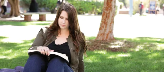 Female student reading a book under a tree